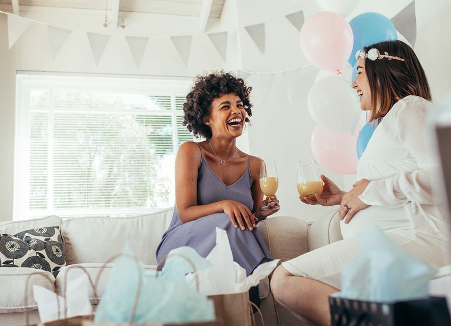 Pregnant woman and friend laughing together at party, holding glasses of juice