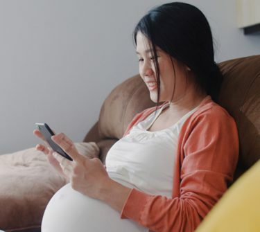 Pregnant woman sitting on sofa and looking at smartphone