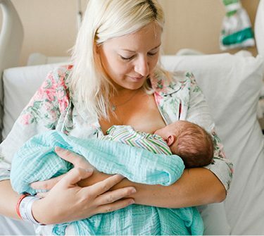Woman breastfeeding baby while sitting in hospital bed
