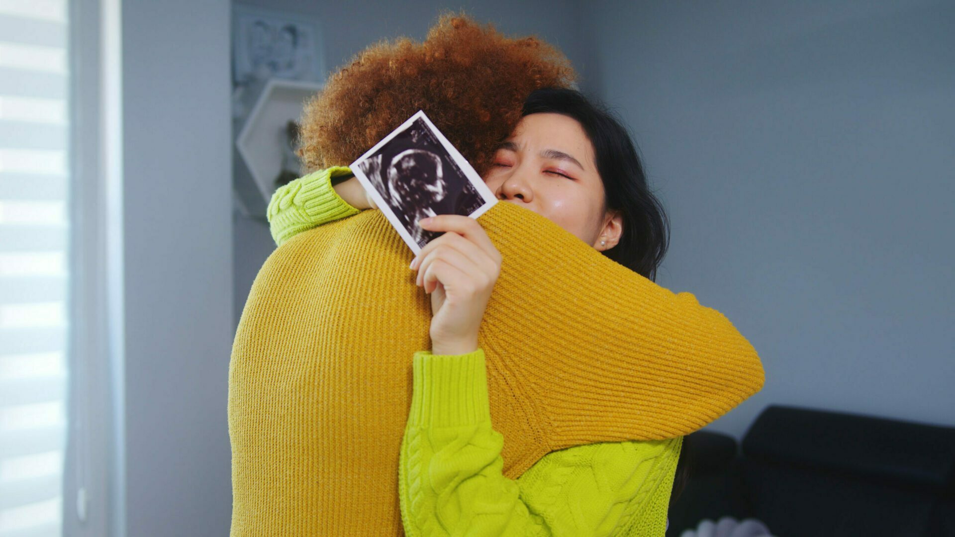 Two people embracing while one holds a fetal ultrasound photo