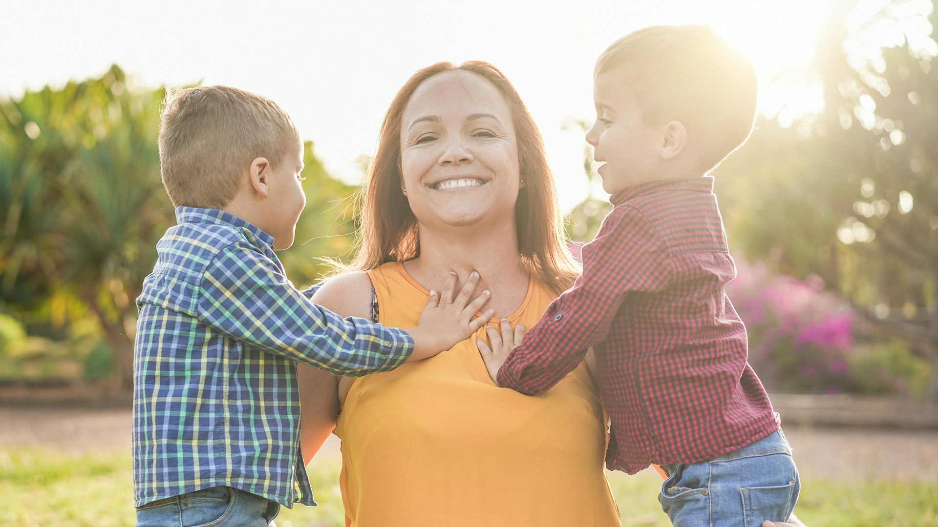 Woman outside looking to camera with two young boys standing on either side and looking at her