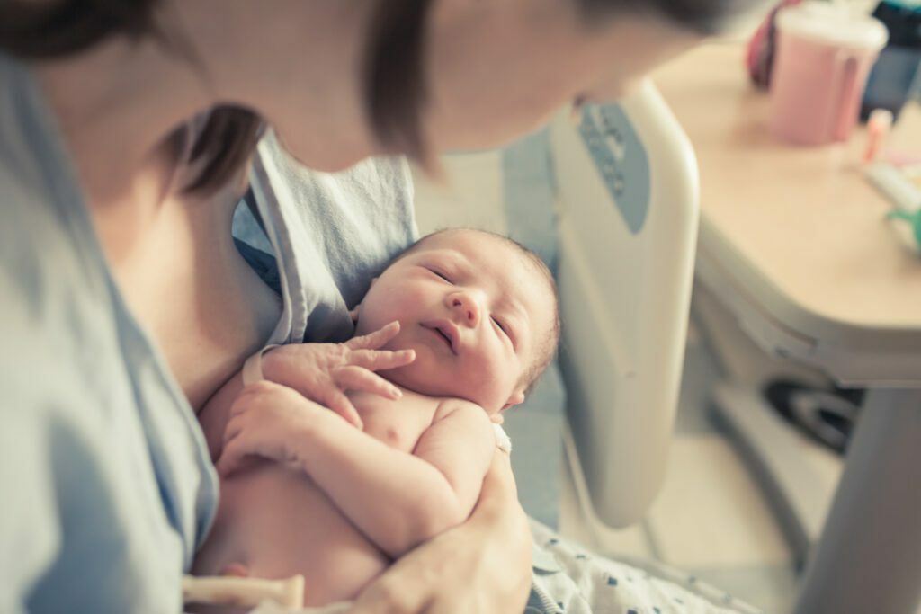 Woman sitting in hospital bed, holding and looking at baby